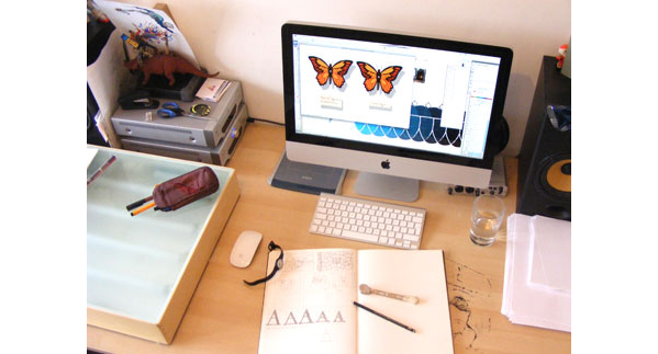 Photo of Adam's old "studio" - showing a desk with sketch book and computer showing illustrations
